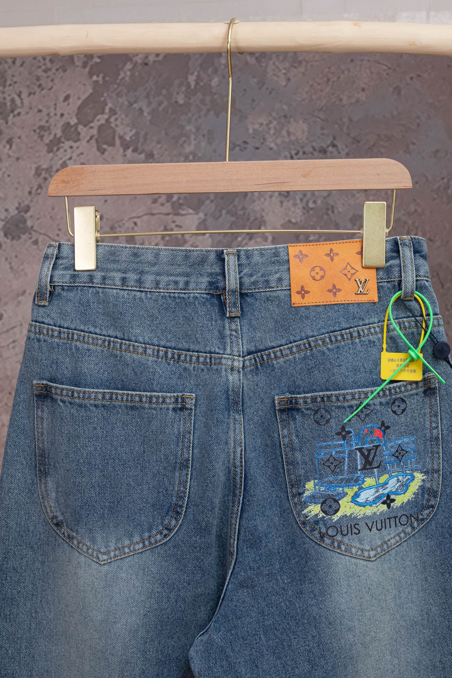 Blue denim jeans with large graphic patch on right back pocket and orange LV tag.