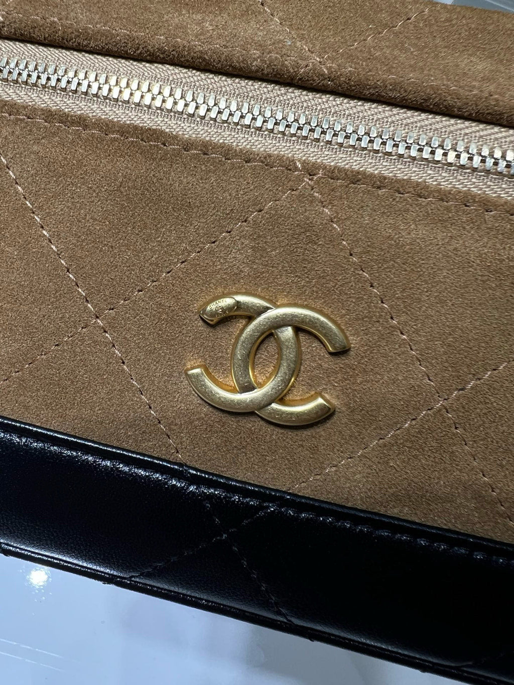 Close-up of gold Chanel logo on suede-style flap with zipper track