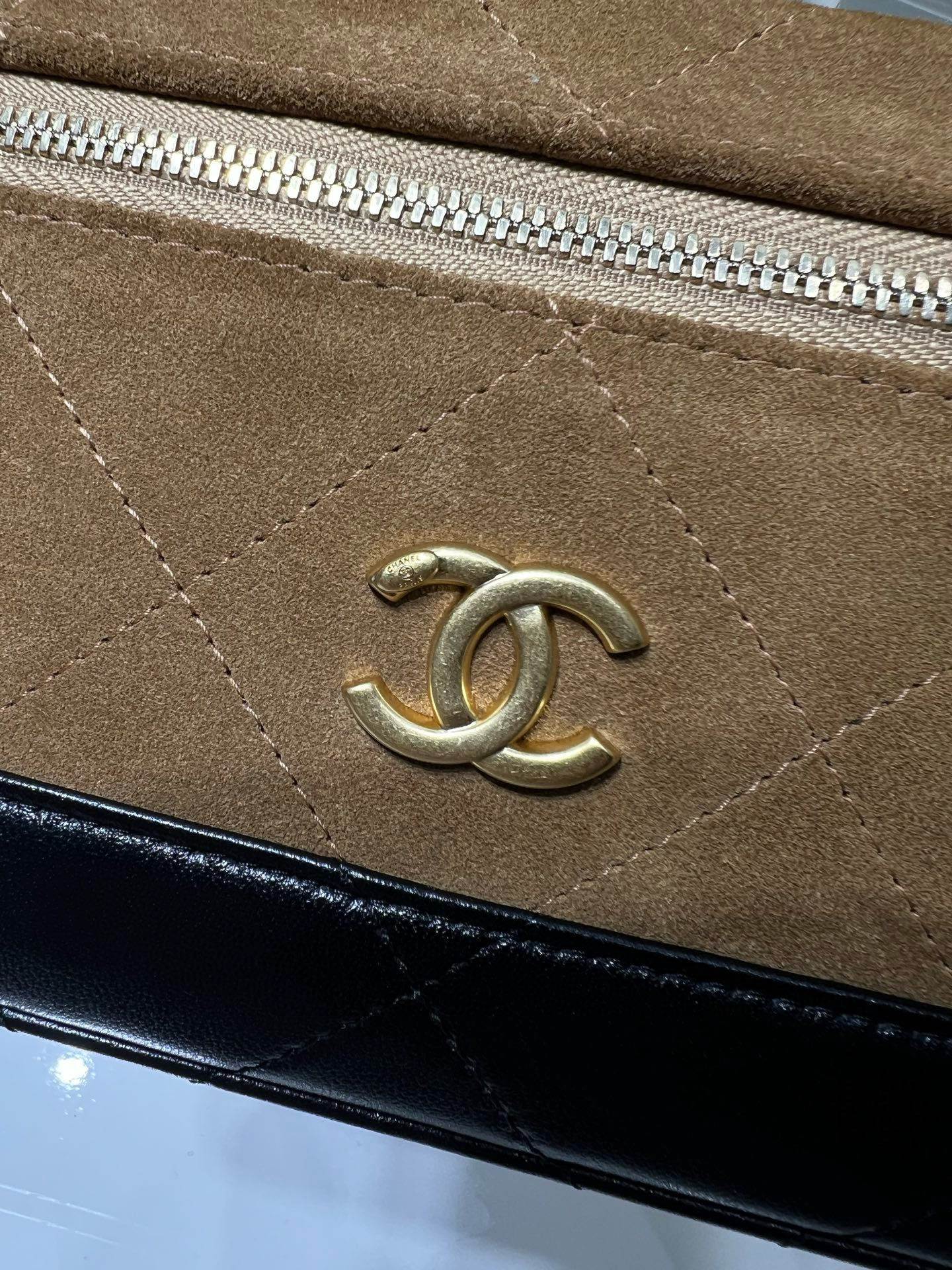 Close-up of gold Chanel logo on suede-style flap with zipper track
