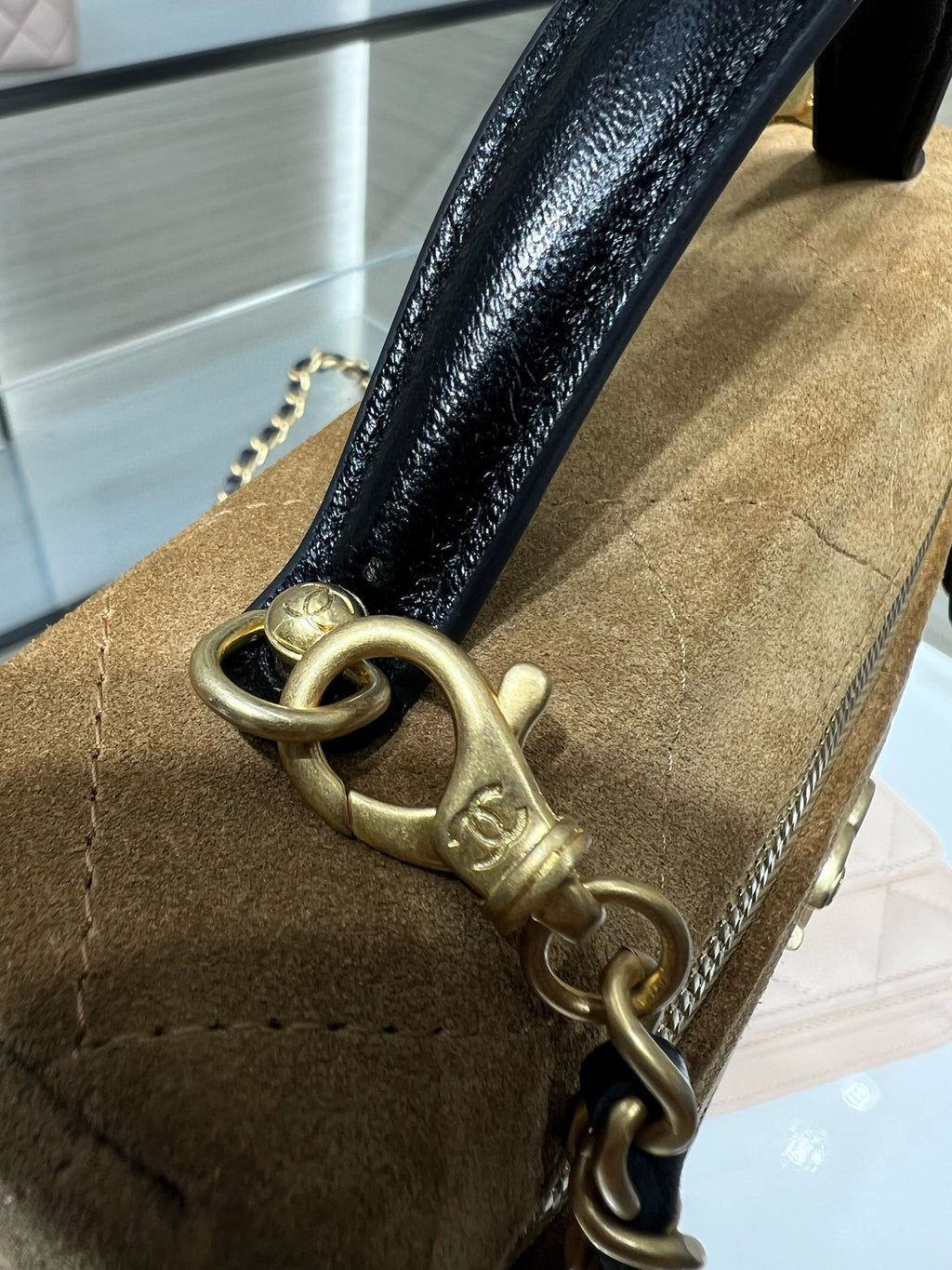 Close-up of Chanel gold-tone chain hardware on gold suede-style bag with black handle