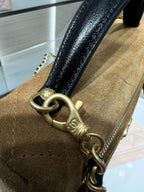 Close-up of Chanel gold-tone chain hardware on gold suede-style bag with black handle