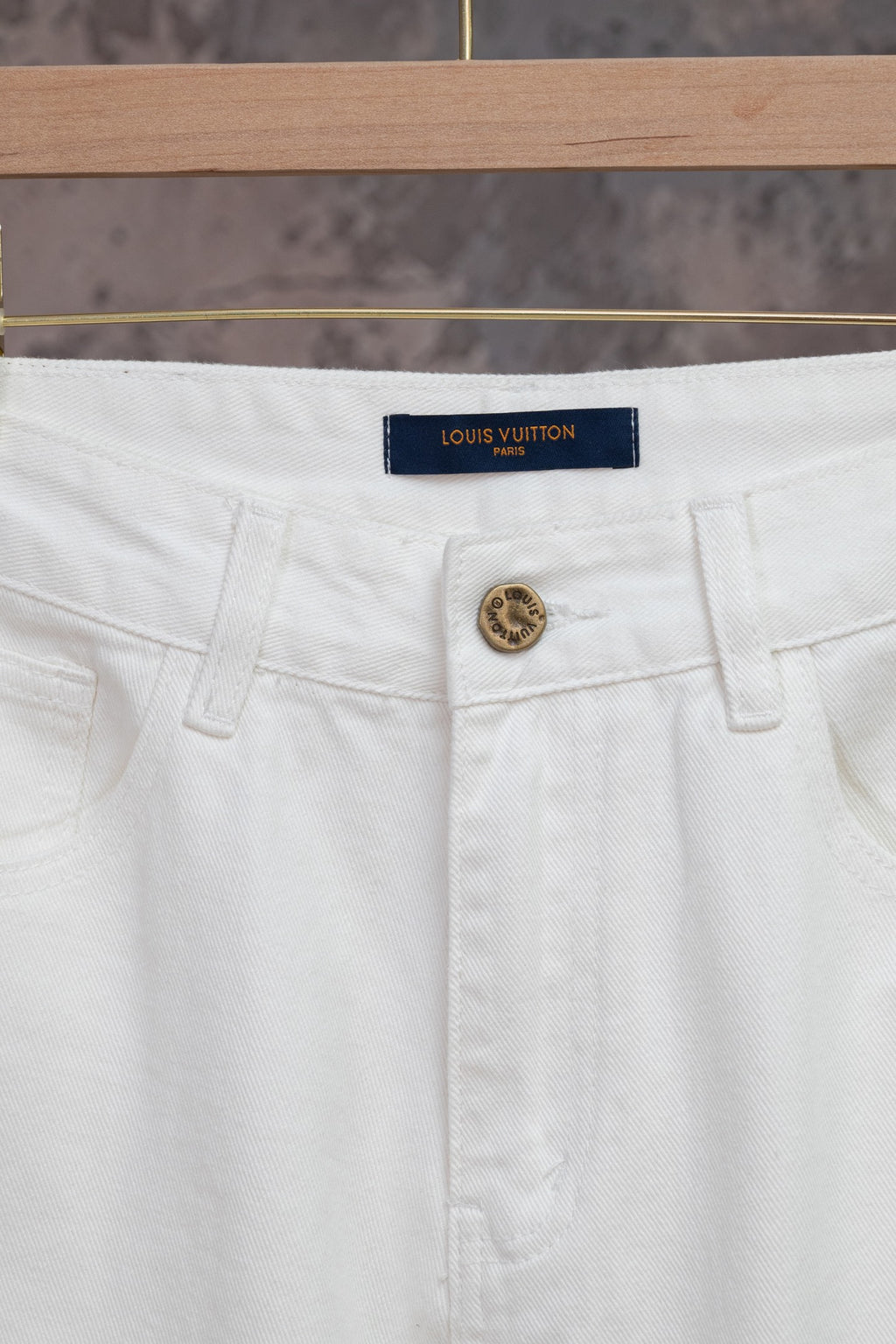 White Louis Vuitton pants close-up: logo waistband tag, button front and pockets