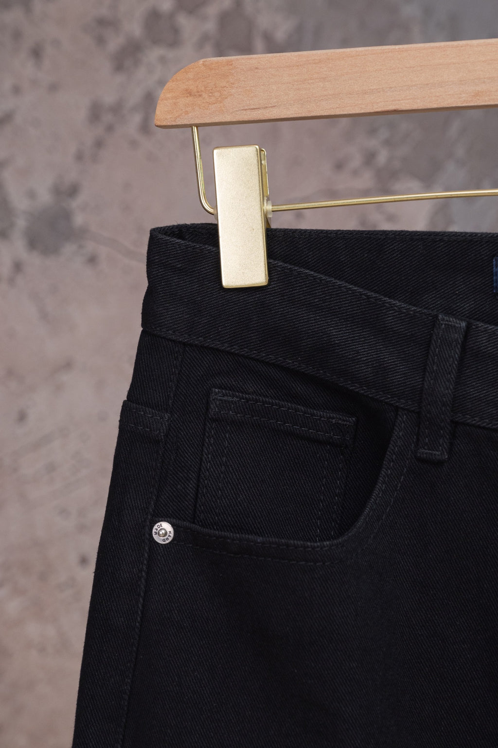 Black denim pants with back waistband and stitched back pocket, close-up