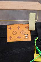 Black denim pants with orange logo patch on waistband, close-up