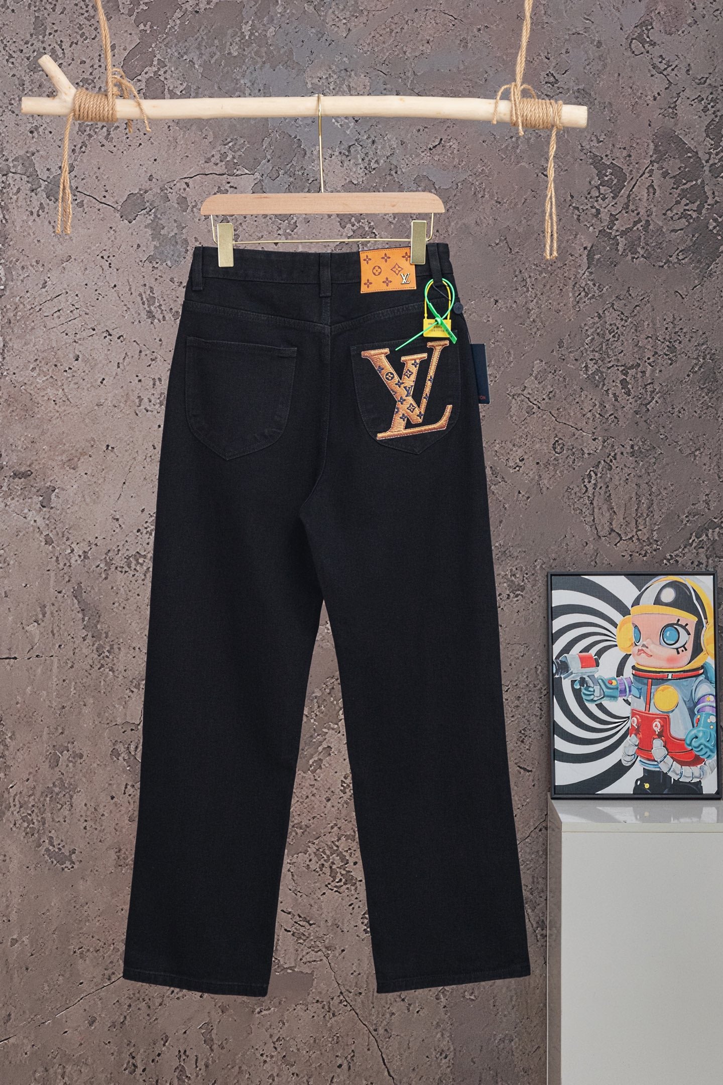 Black denim pants with front button and belt loops, hanging on a wooden hanger