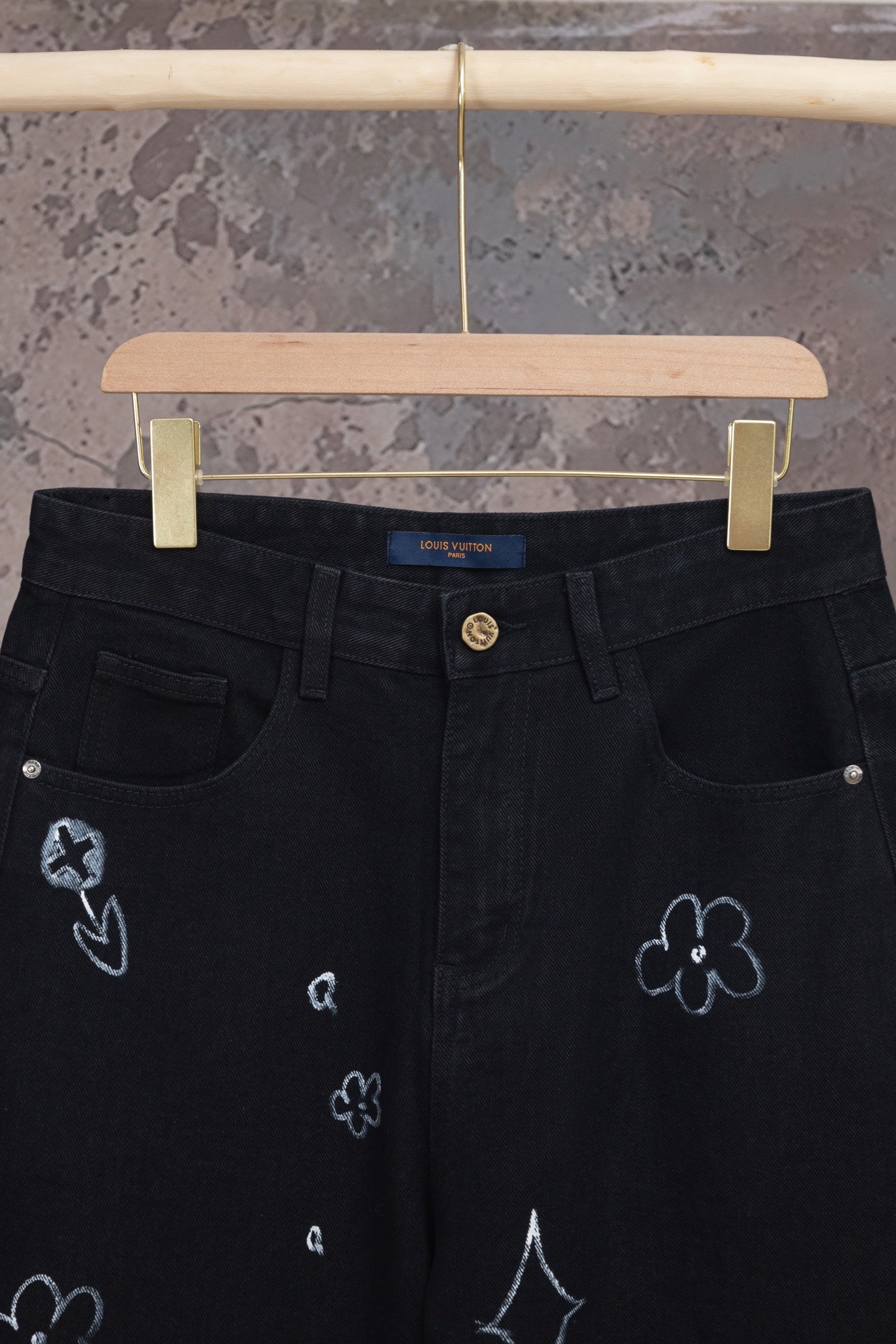 Black denim pants with button waistband and embroidered icons on legs