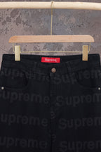 Black denim pants waist close-up with red Supreme label and button
