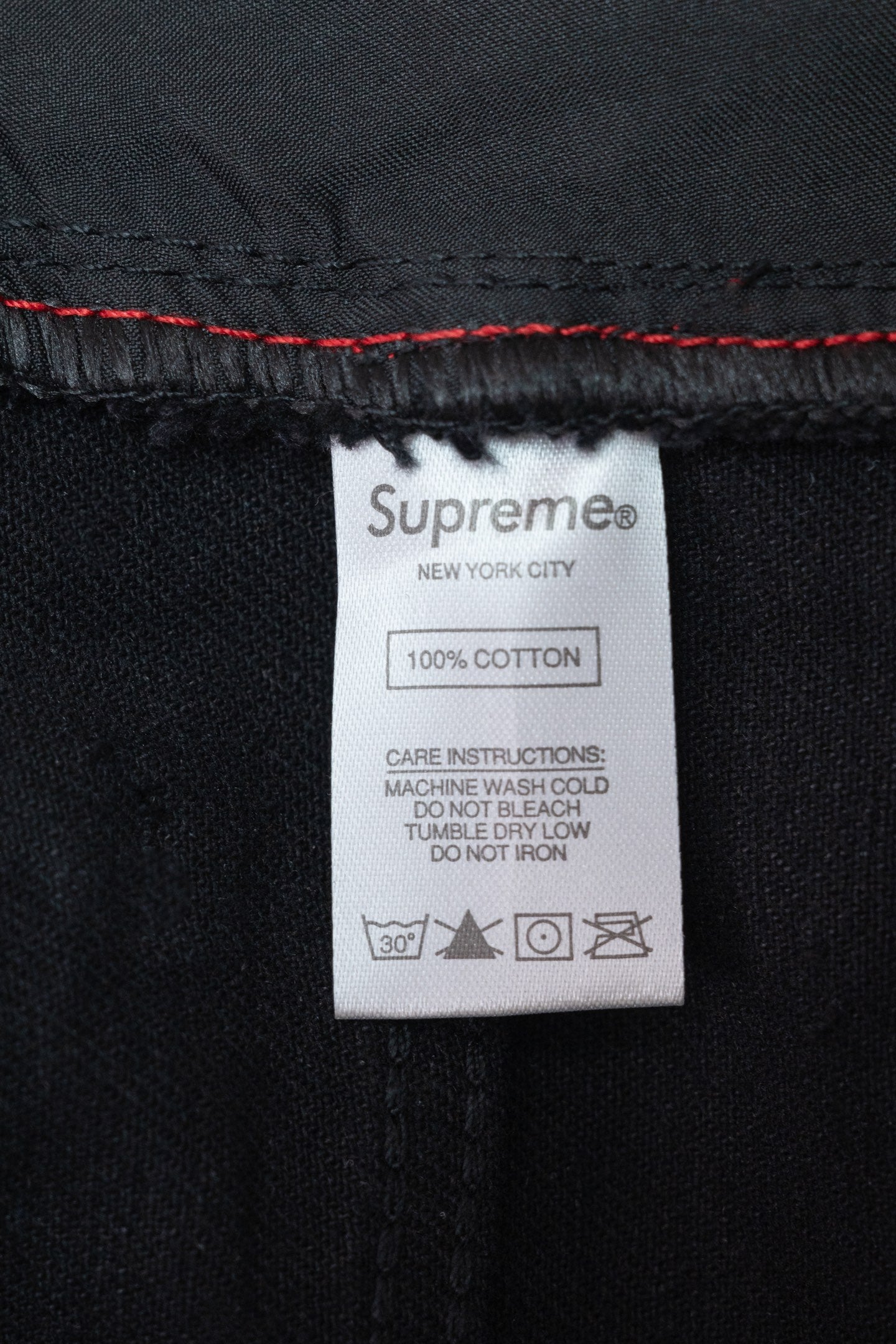 Black denim pants care label showing Supreme and 100% cotton