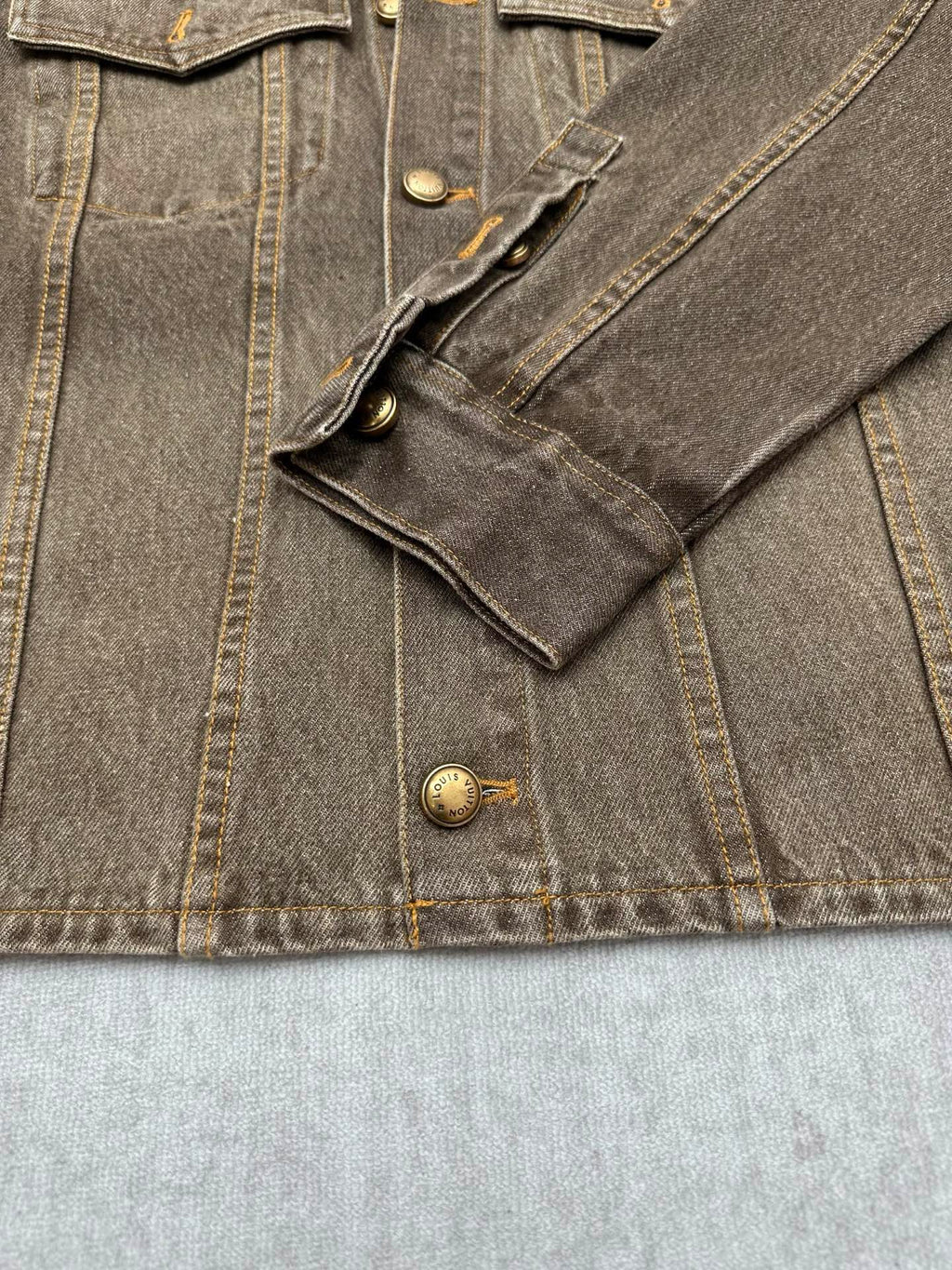 Dark gray denim jacket pocket and button details with visible stitched seams