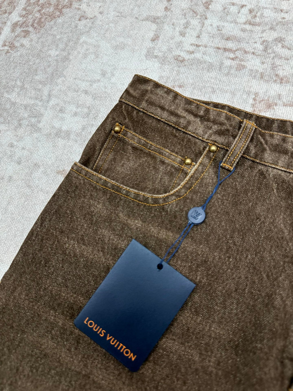Brown denim jeans waistband detail with blue cord, gold rivets, and Louis Vuitton tag