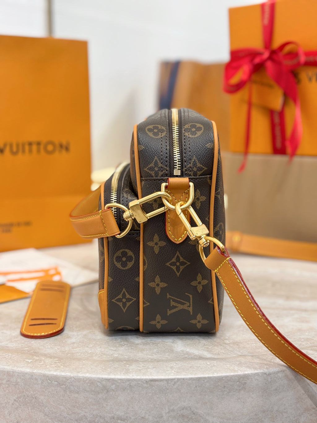 Louis Vuitton monogram bag with front zipper, tan leather trim, and gold chain strap