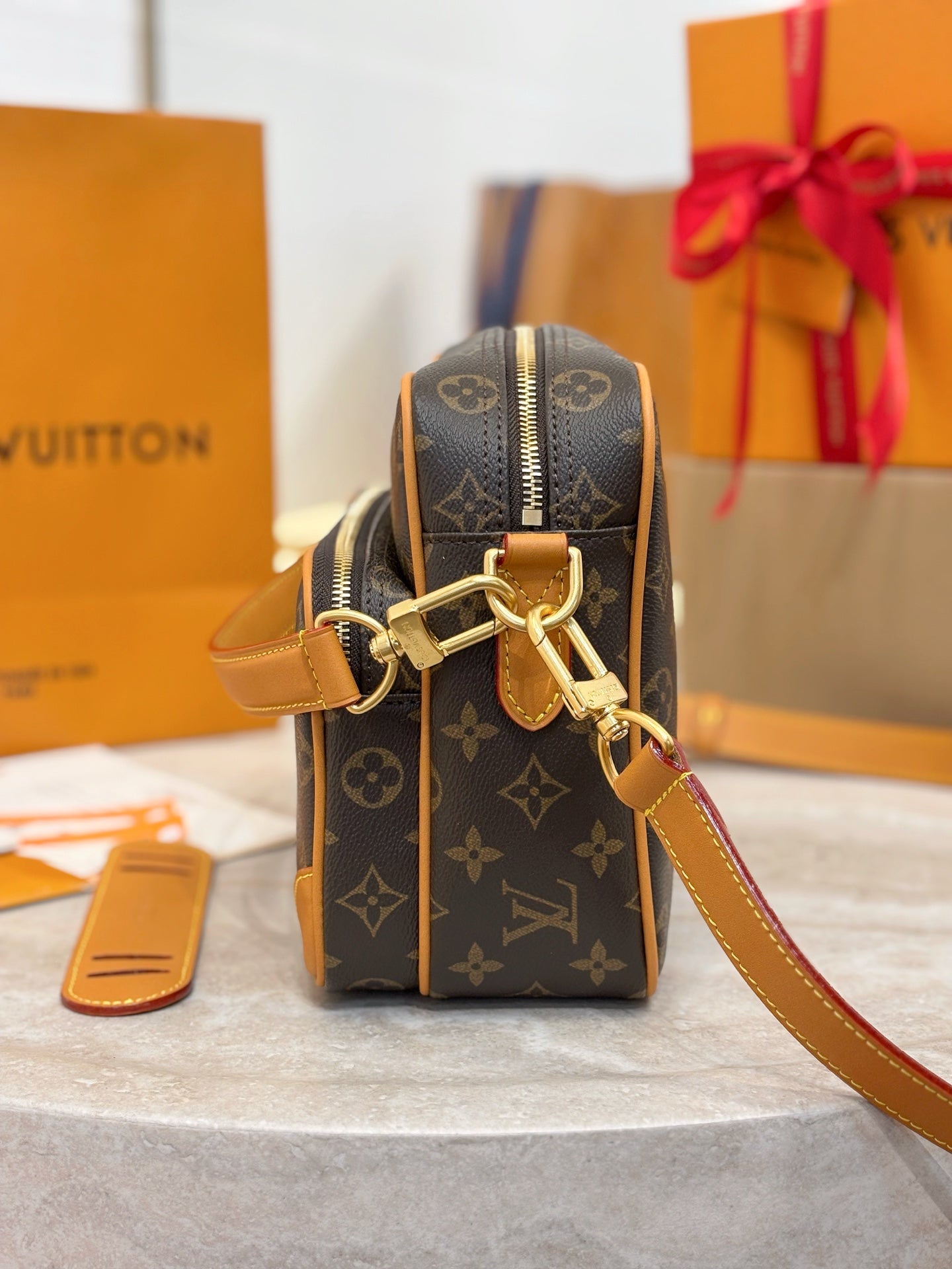 Louis Vuitton monogram bag with front zipper, tan leather trim, and gold chain strap