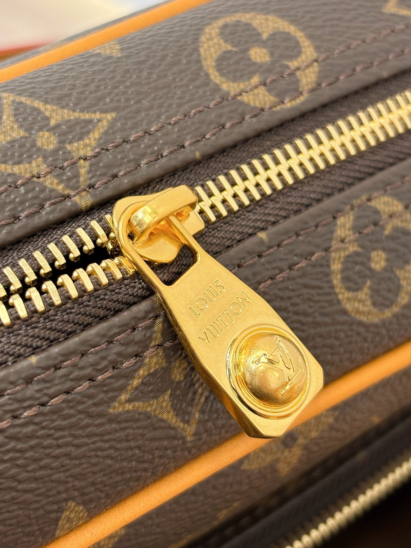 Gold zipper pull on Louis Vuitton monogram bag with tan-trim zipper track