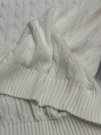 White cable-knit sweater vest close-up showing knit texture and ribbed edge