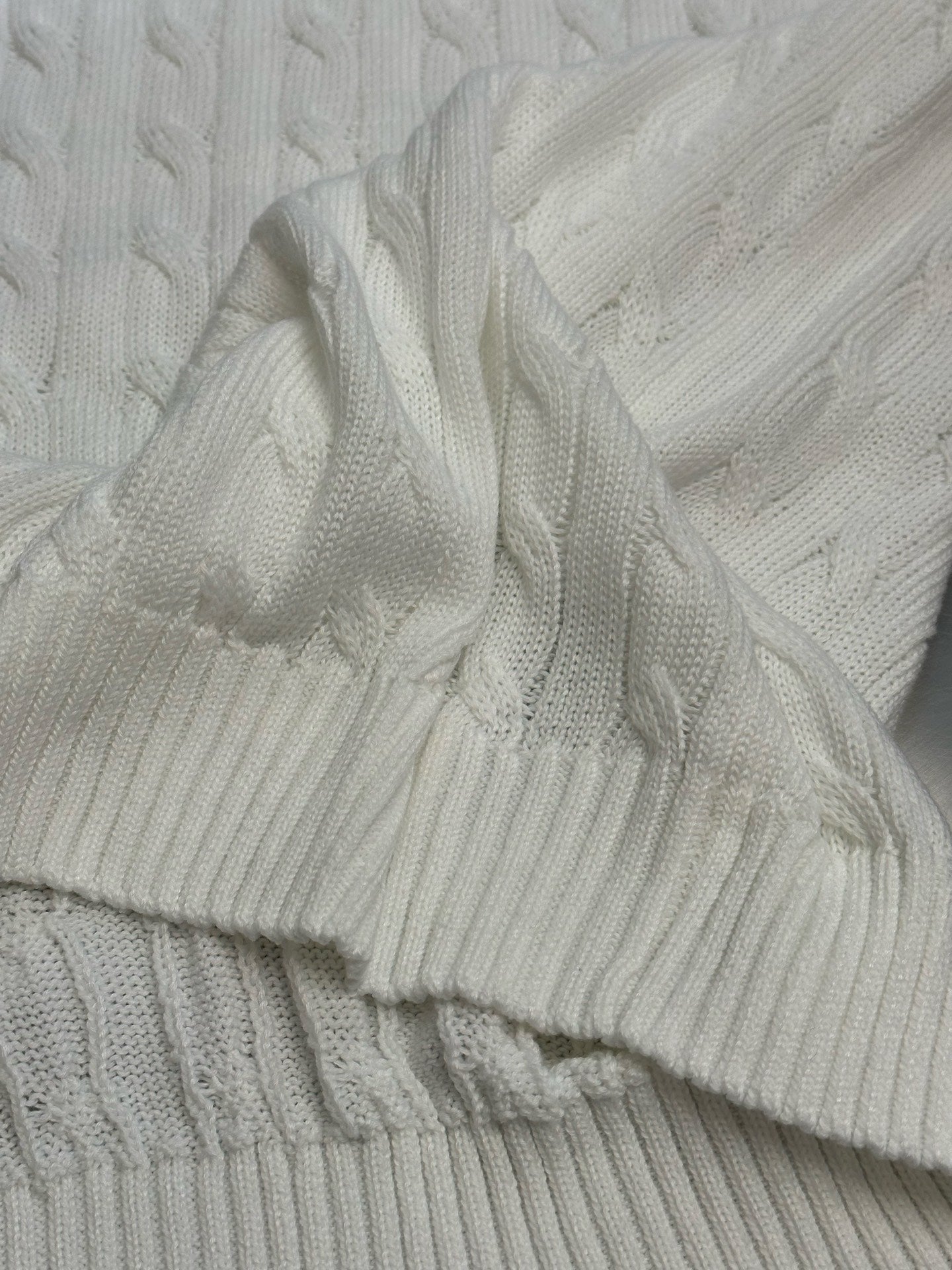 White cable-knit sweater vest close-up of ribbed cuff and hem