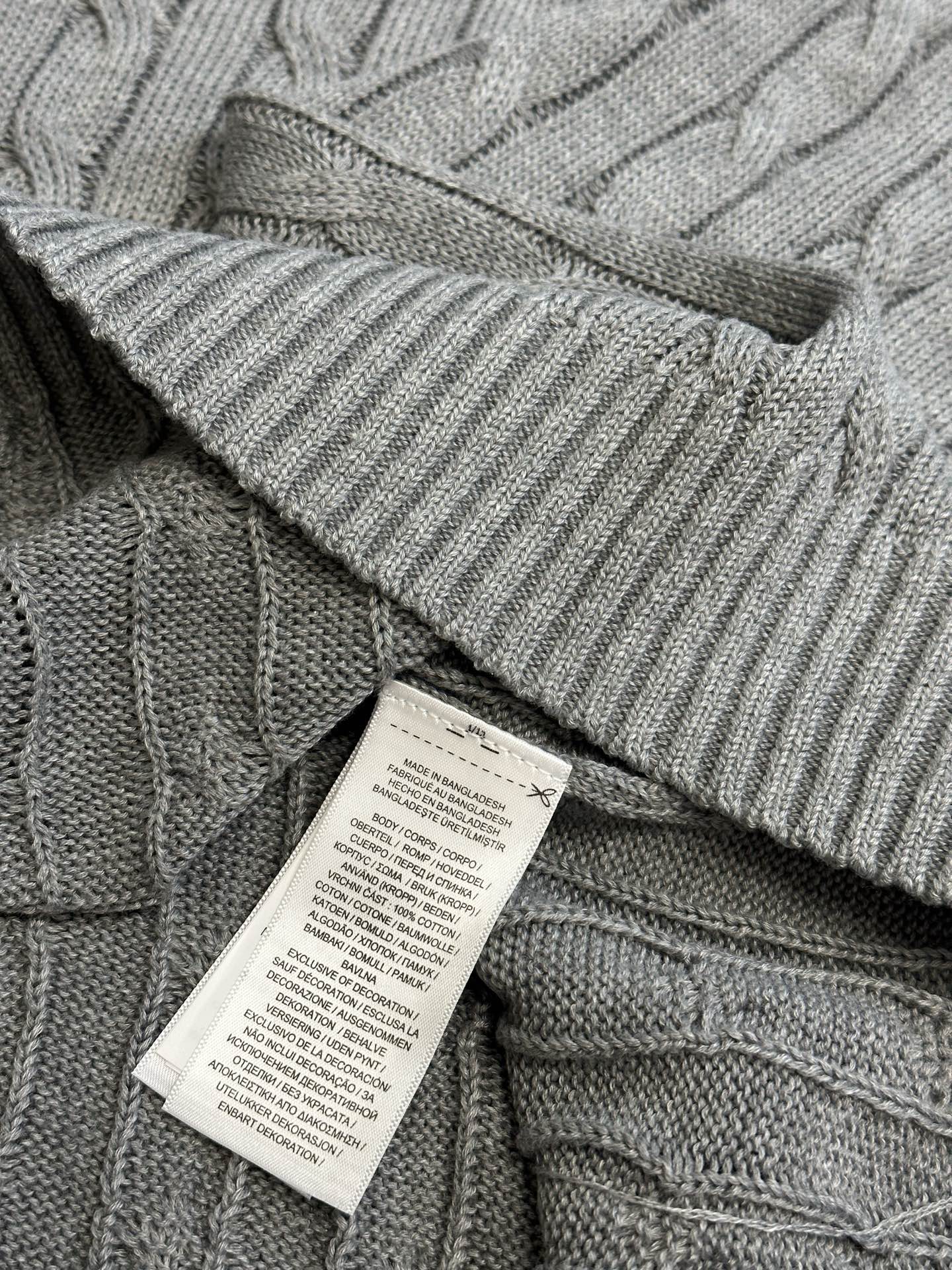 Gray cable-knit sweater vest hem with ribbed edge and care label