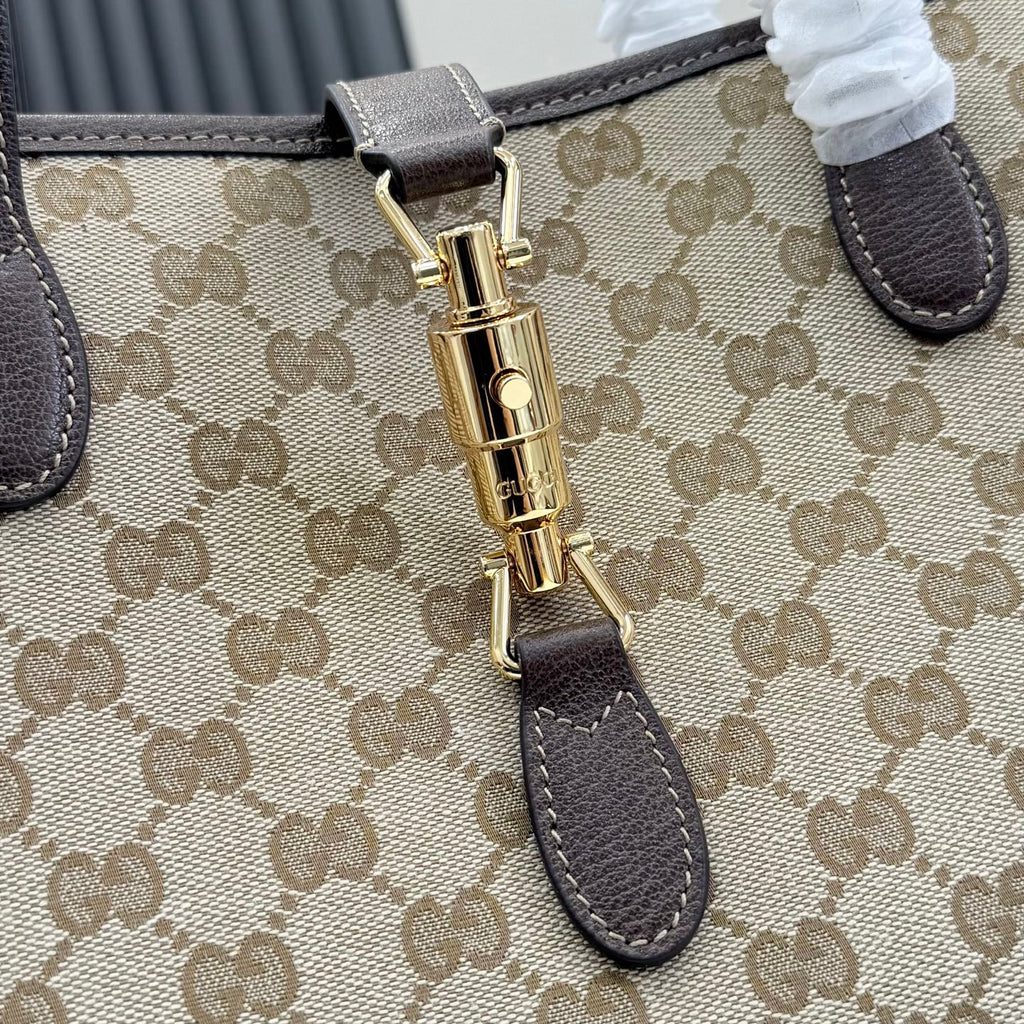 Close-up of beige GG monogram tote bag clasp with gold hardware and dark brown leather strap.