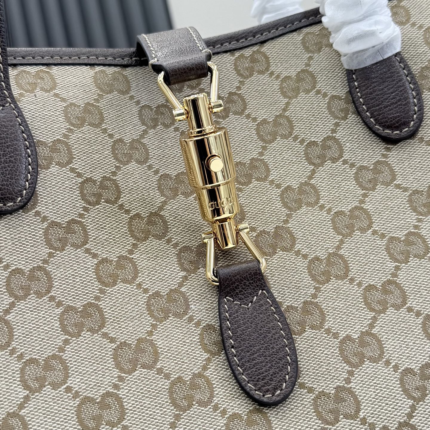 Close-up of beige GG monogram tote bag clasp with gold hardware and dark brown leather strap.