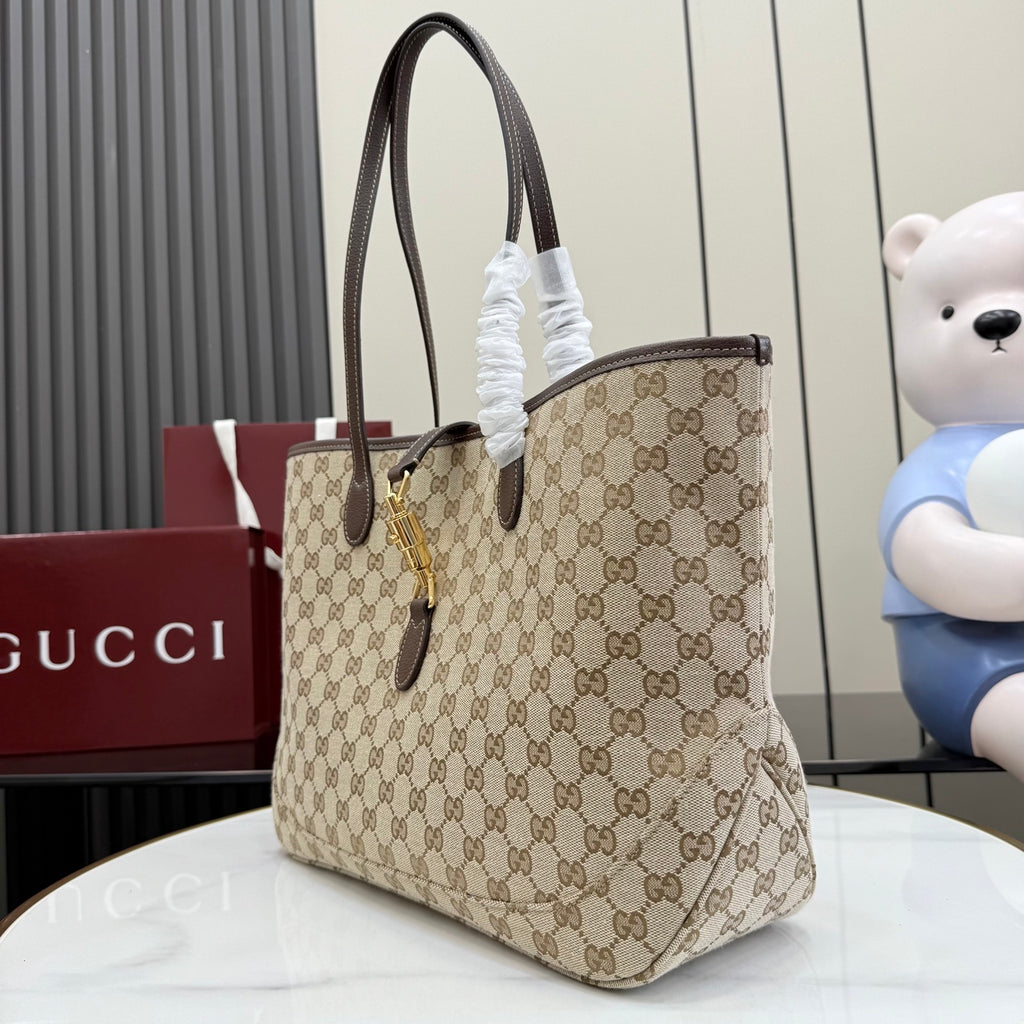 Beige GG monogram tote bag with dark brown leather handles and gold lock hardware.