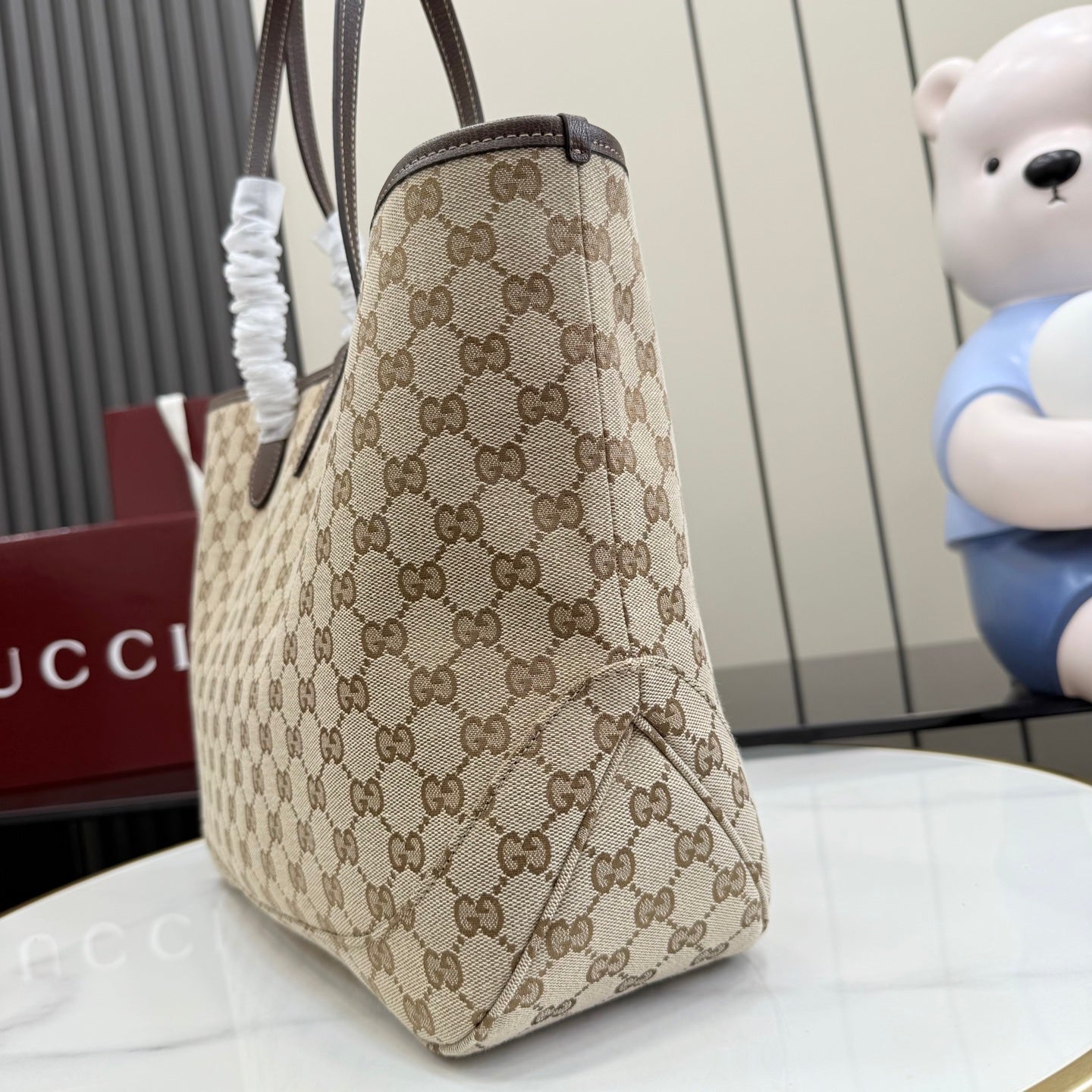 Beige GG monogram tote bag viewed from side/back with dark brown trim and top handle.