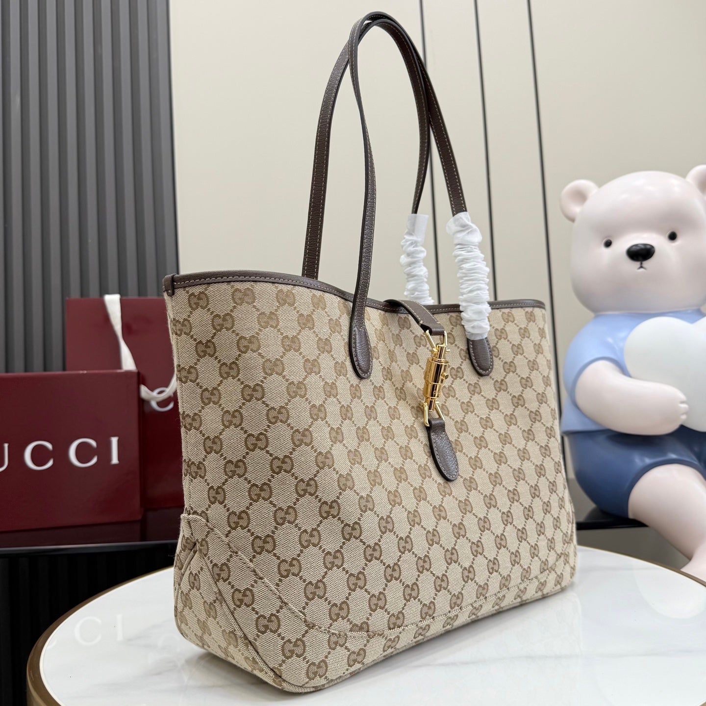 Beige GG monogram tote bag with dark brown leather straps and gold lock hardware.