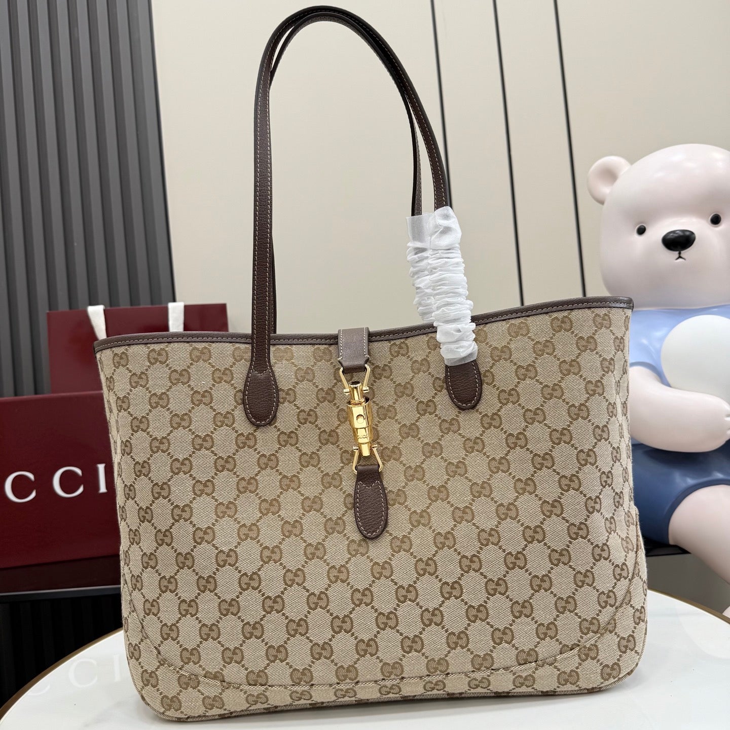 Tote bag with beige GG monogram canvas, dark brown leather handles, and gold clasp hardware.