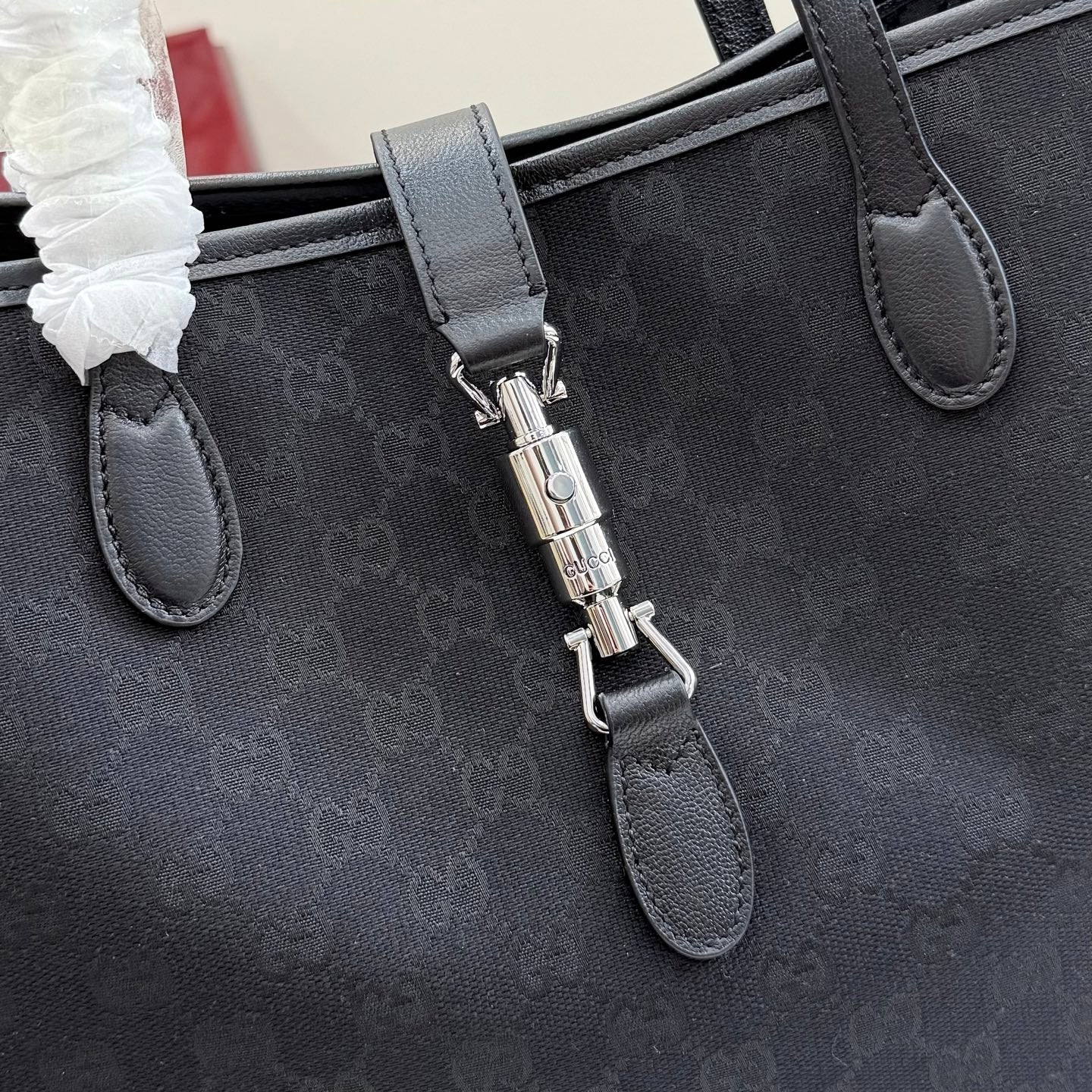 Gucci tote bag close-up of leather strap tabs and metal key holder on GG canvas
