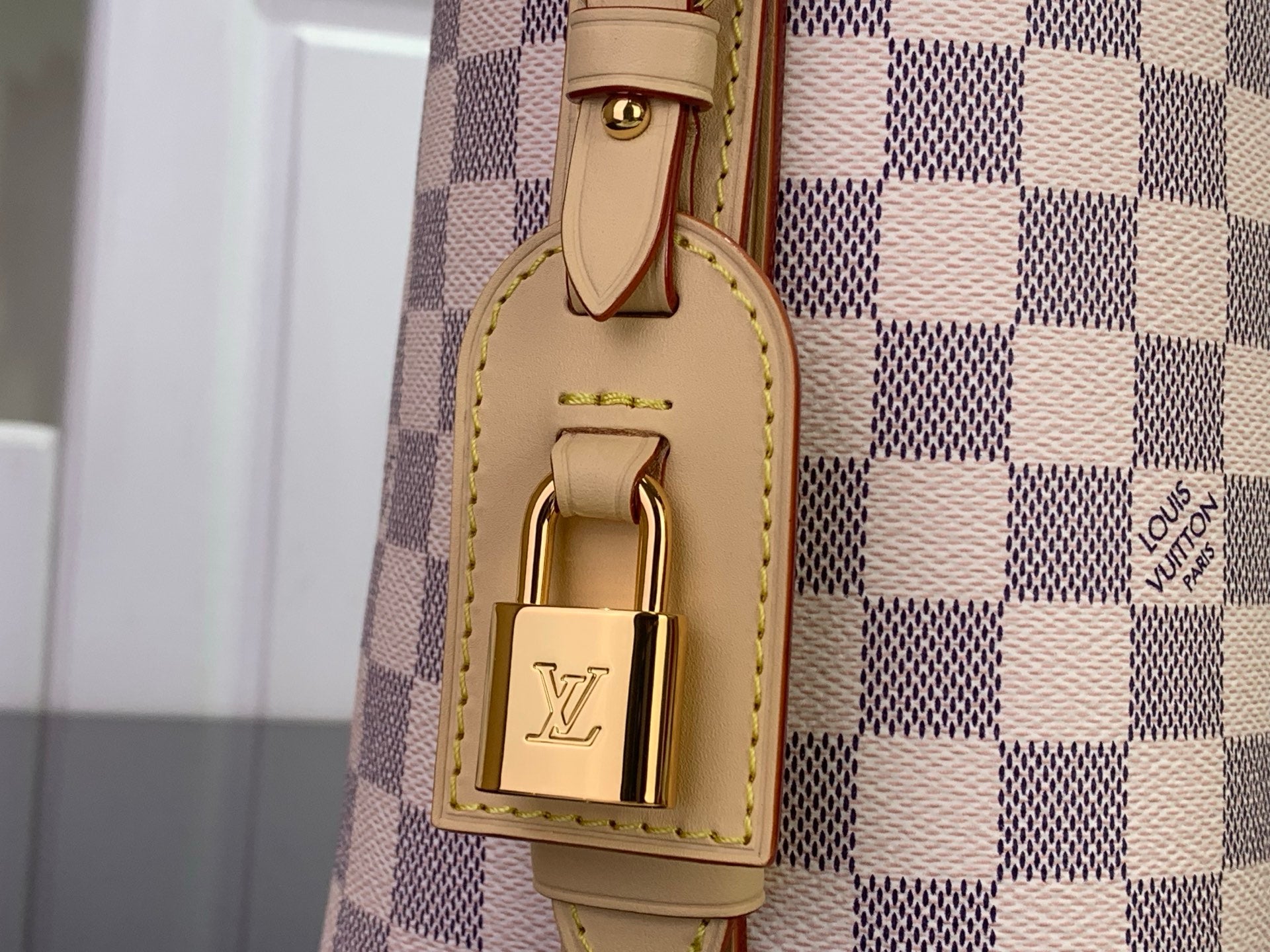 Louis Vuitton lock detail on tan leather strap attached to checkered bag panel