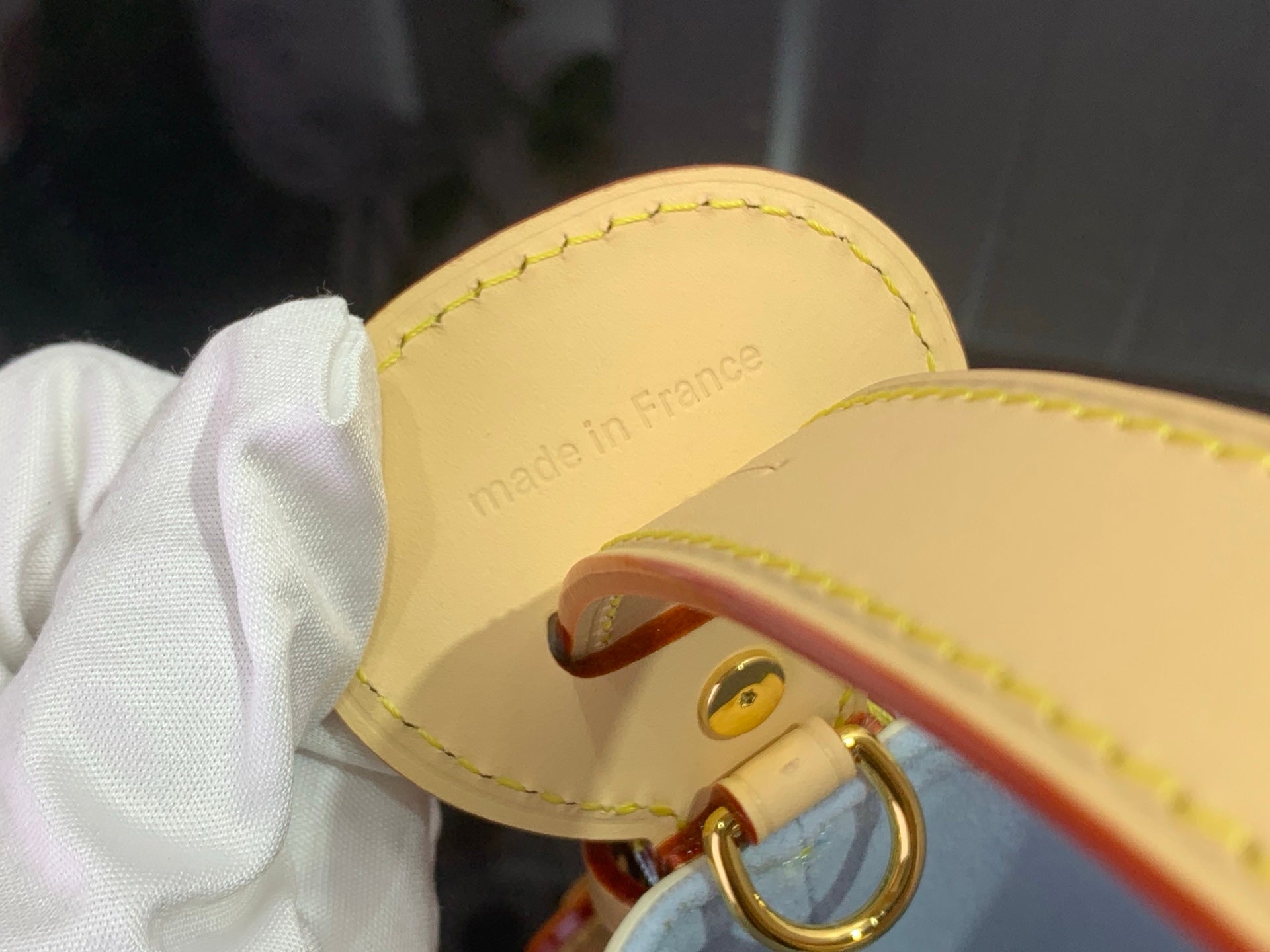Leather strap end with gold eyelet and “made in France” text, yellow stitching
