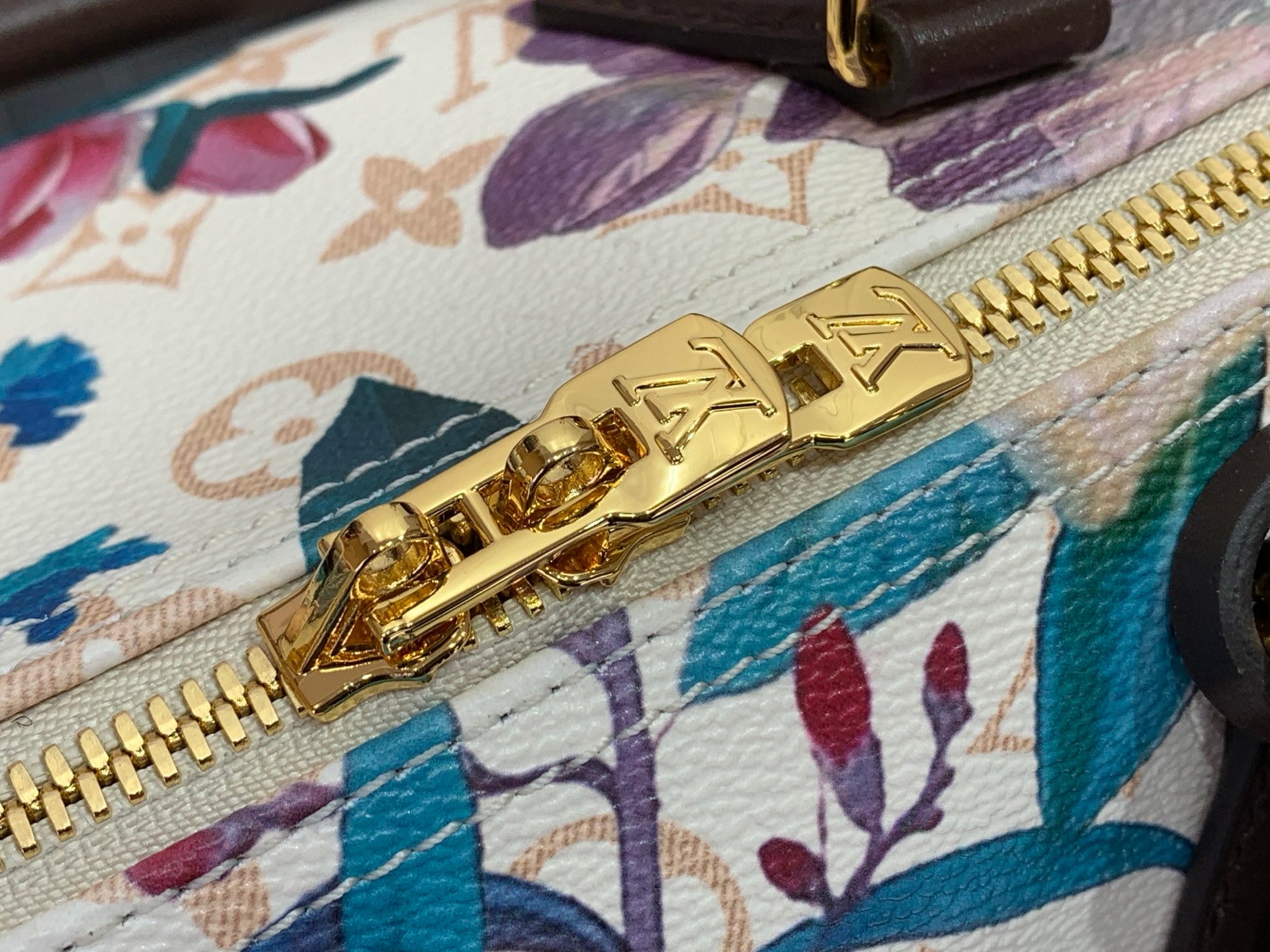 Gold zipper pull on floral handbag with white base, teal and purple designs
