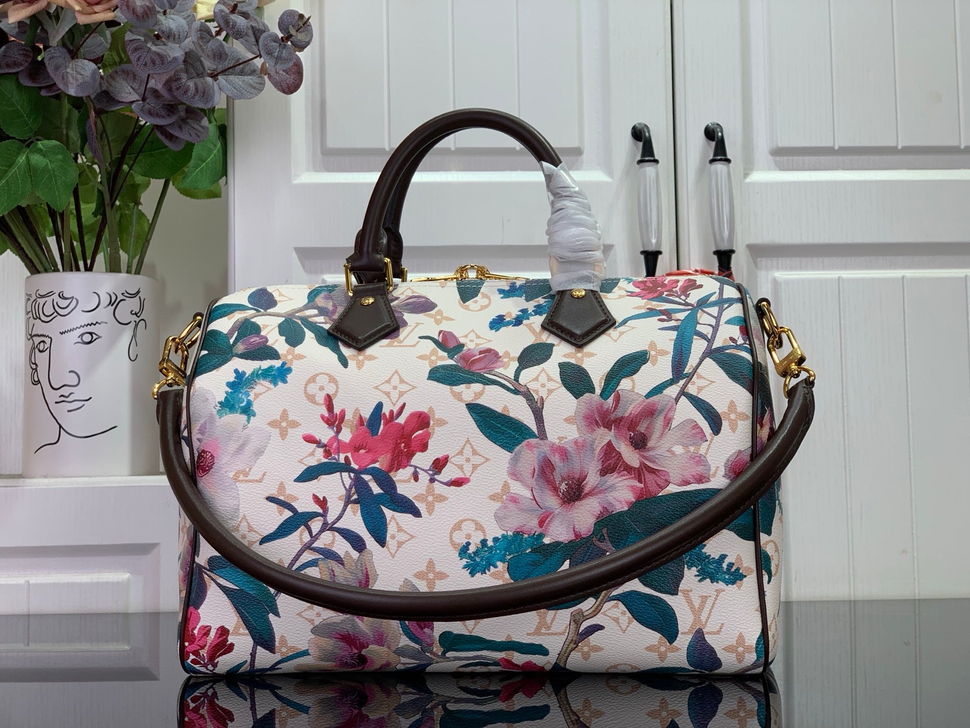Floral handbag with white background, blue and pink flowers, brown handles, gold accents