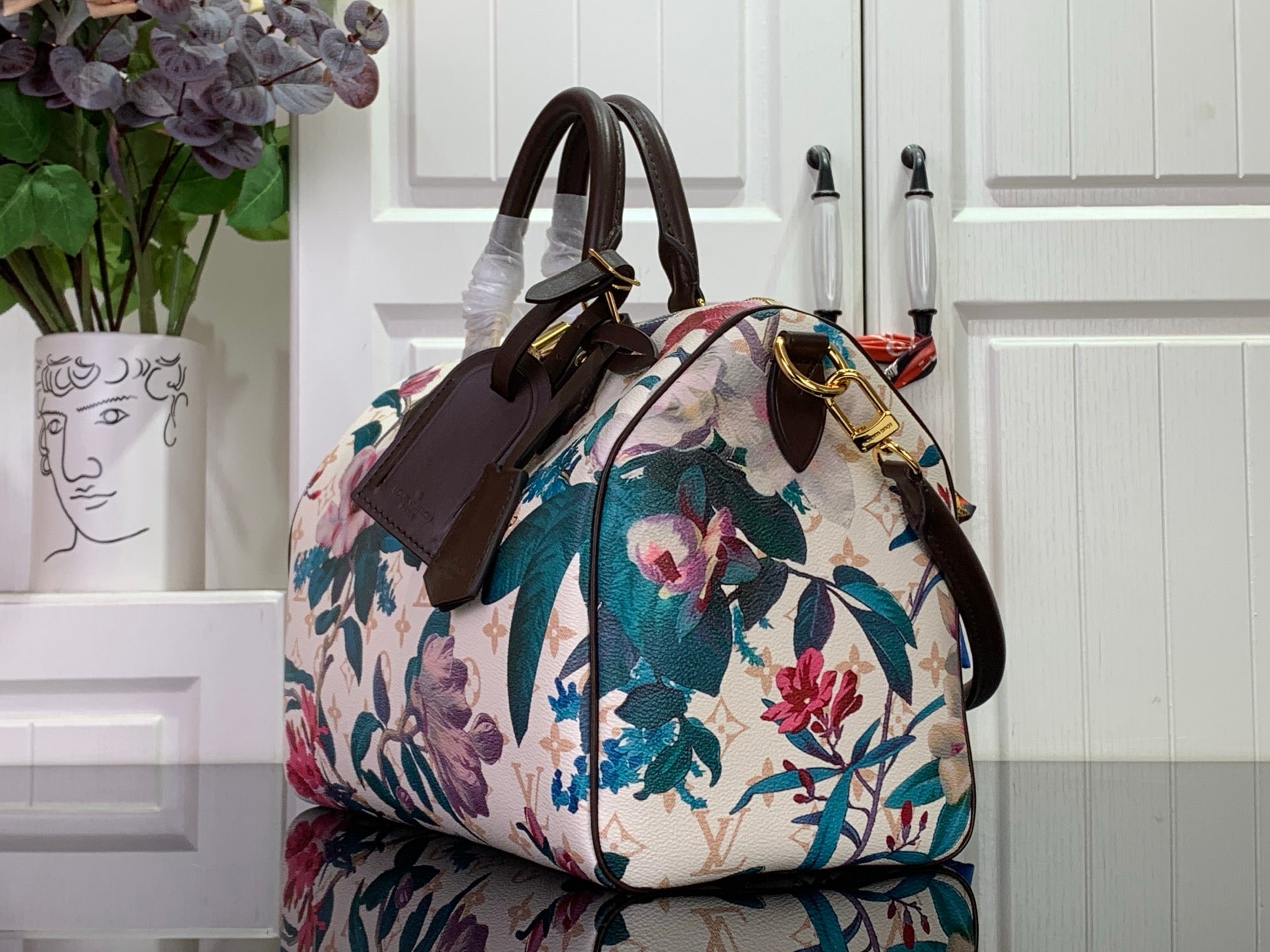 Floral handbag with white base and colorful blossoms, brown top handle, gold hardware