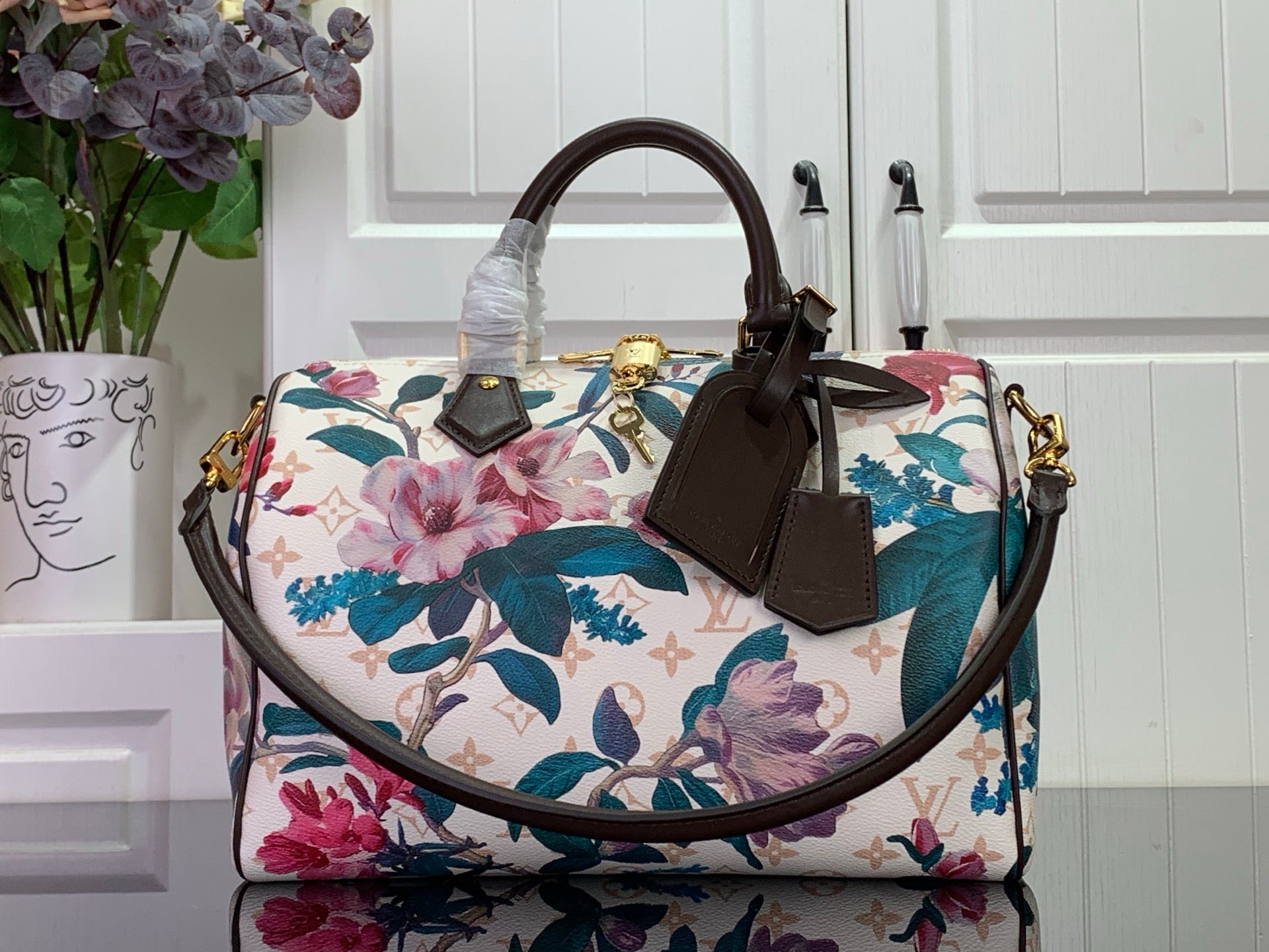 Louis Vuitton handbag with floral print, white base, teal and pink flowers, brown handles
