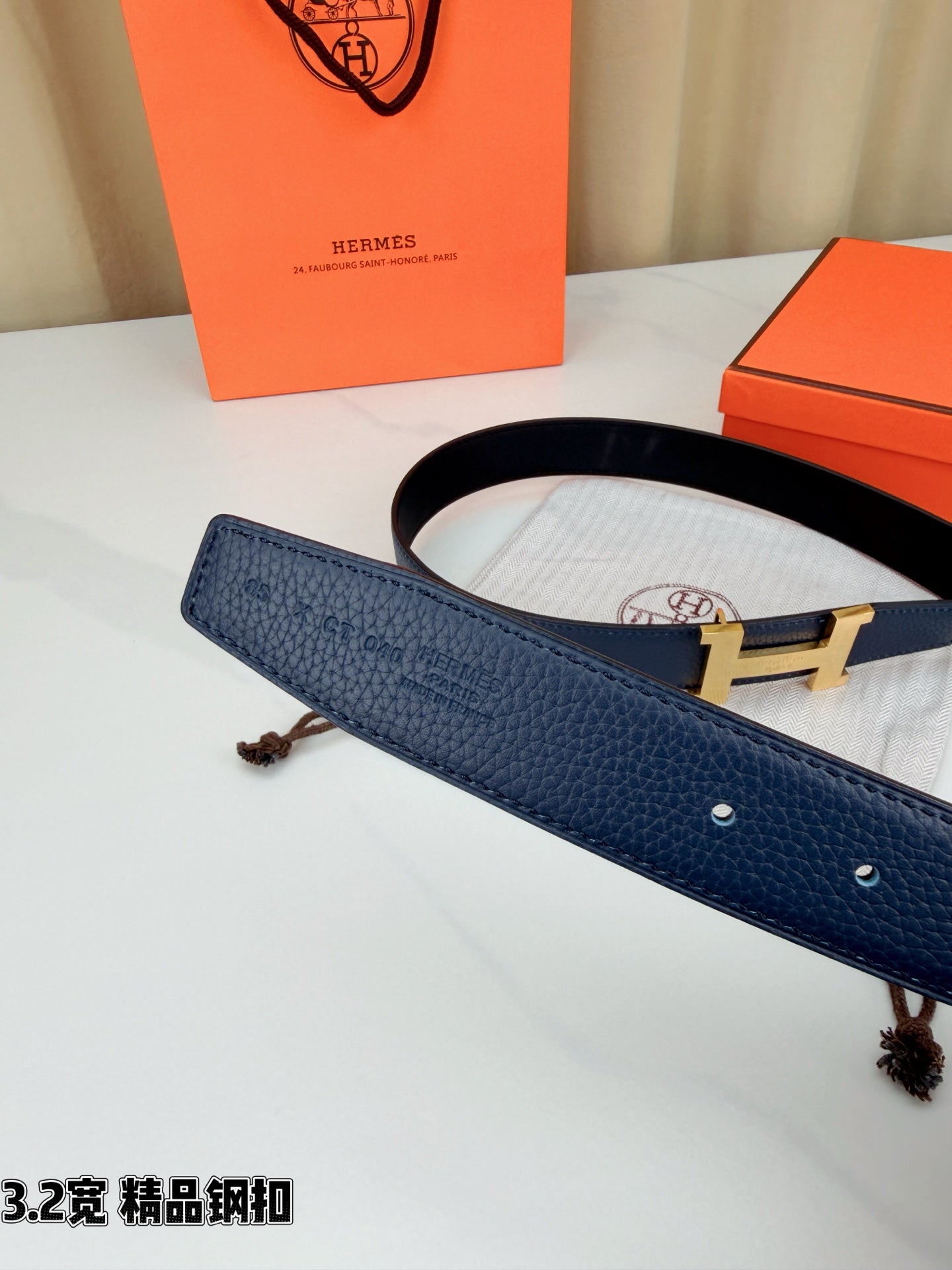 Dark blue leather belt with gold H buckle, strap with small holes visible