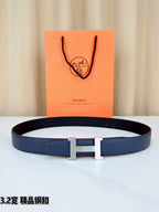 Dark blue leather belt with gold H buckle, laid flat on a white surface