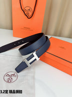 Dark blue leather belt with gold H buckle, laid across an open orange box