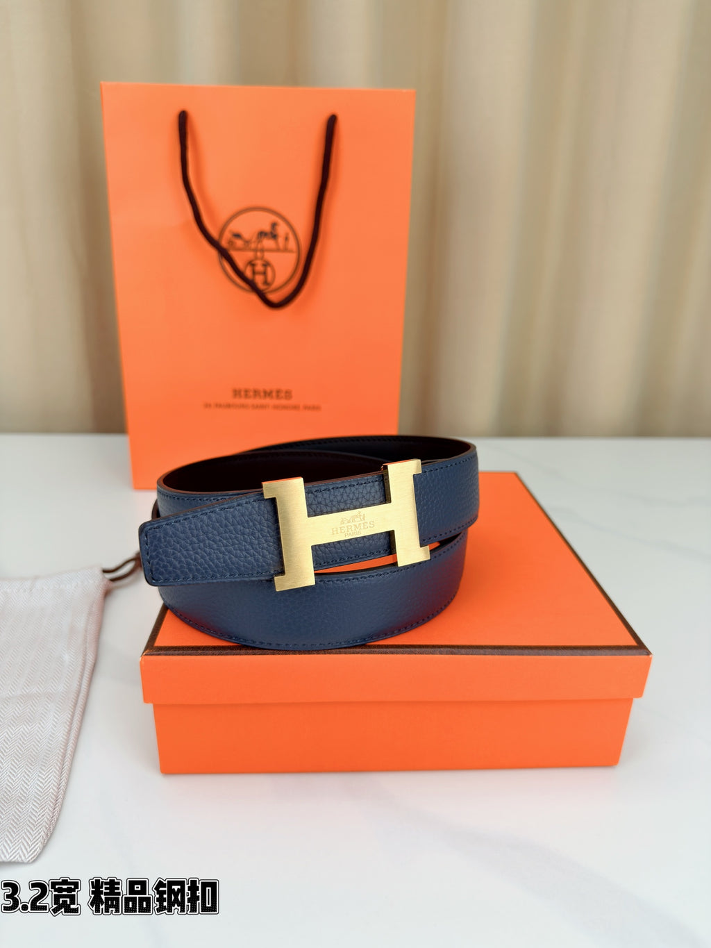 Dark blue leather belt with gold H buckle, resting on an orange box