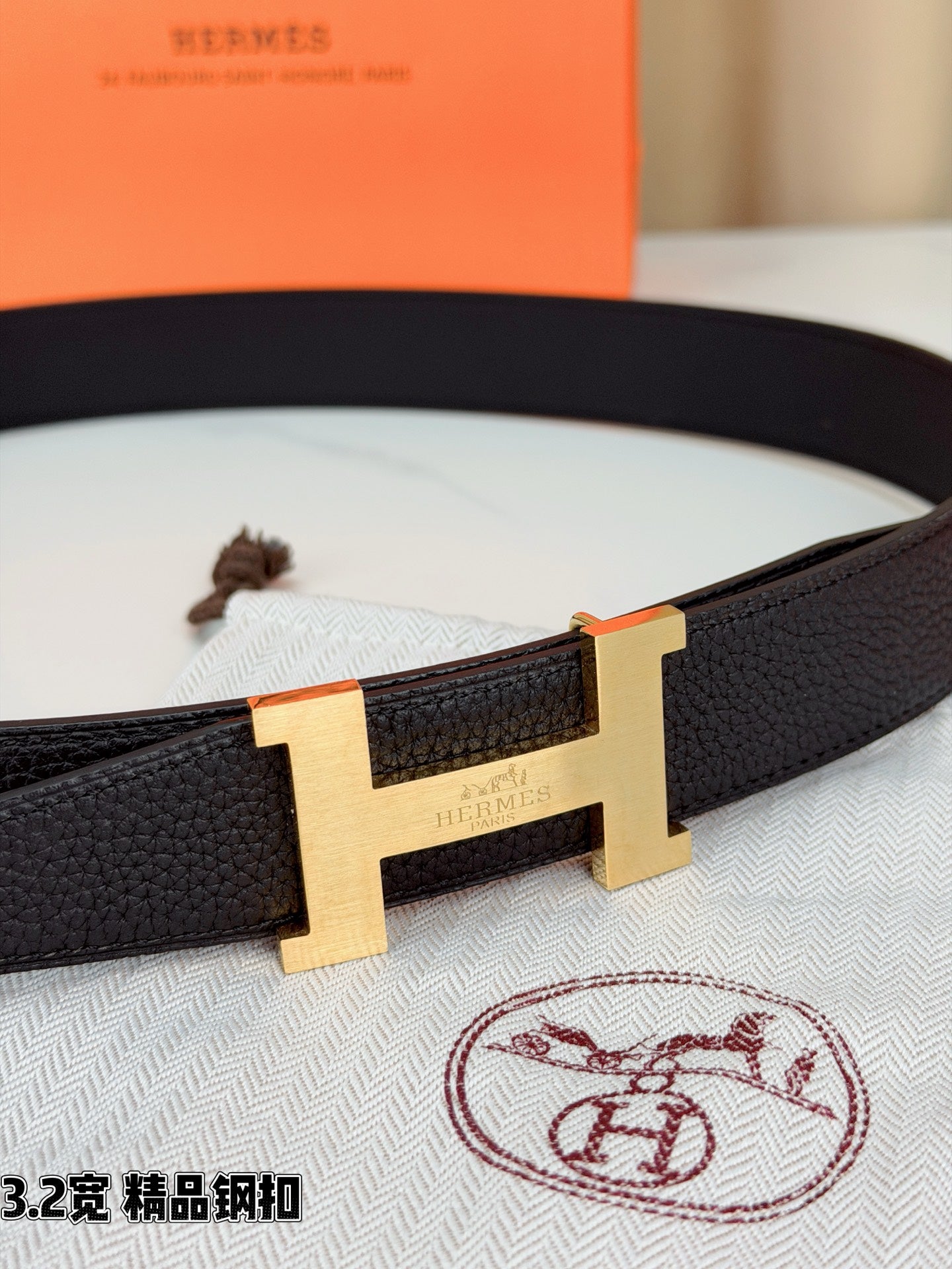 Close-up of dark leather belt with gold-tone H buckle and engraved front.
