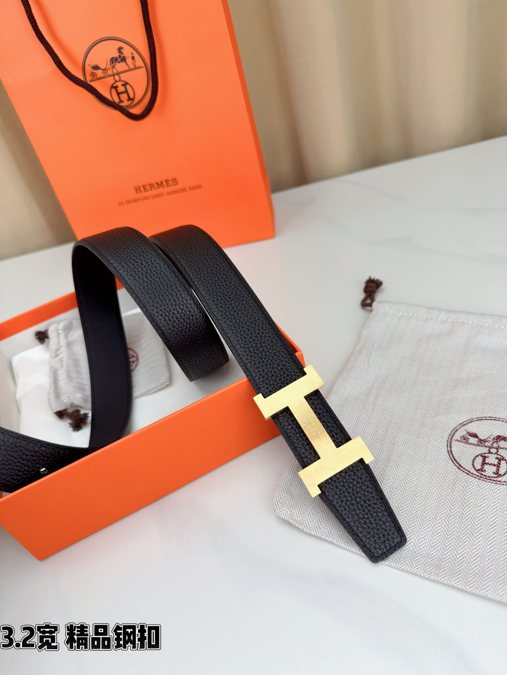 Dark leather belt with gold-tone H buckle, side view with end of strap visible.