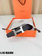 Dark leather belt with gold-tone H buckle, placed on a pouch and fabric.