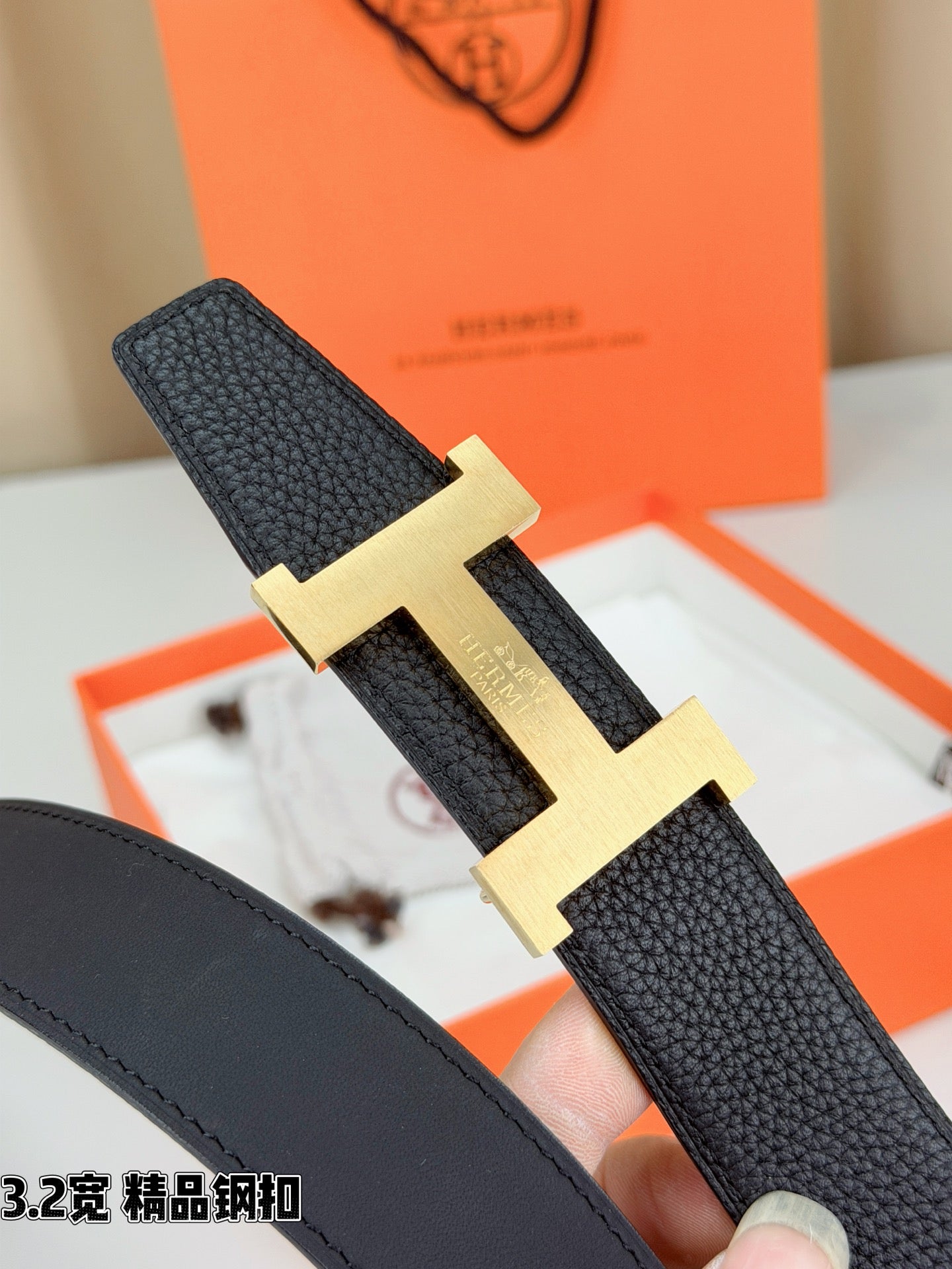 Dark leather belt with gold-tone H buckle, angled view showing textured strap.