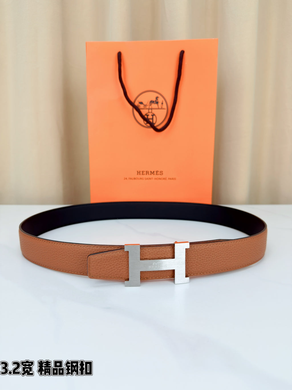 Brown leather belt with gold H buckle, laid flat on a white surface.