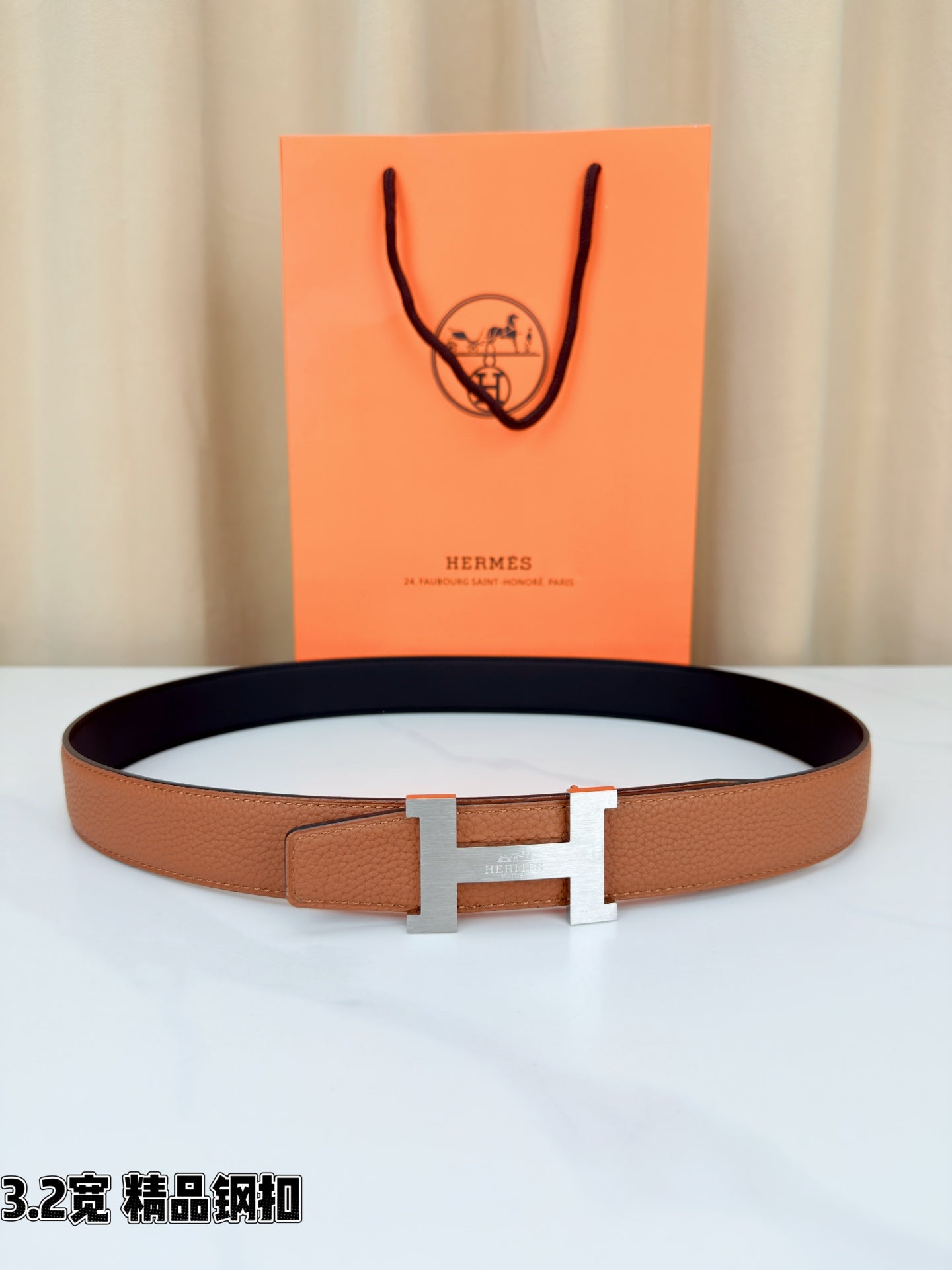 Brown leather belt with gold H buckle, laid flat on a white surface.