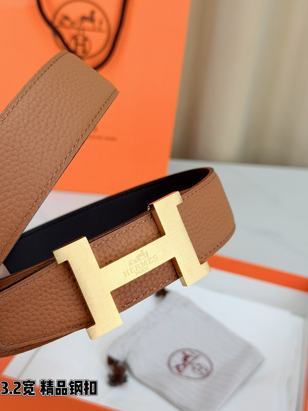 Brown leather belt close-up showing gold H buckle and keeper strap.