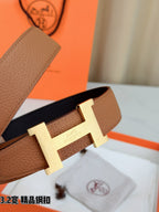 Brown leather belt close-up showing gold H buckle and keeper strap.
