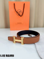 Brown leather belt with gold H buckle resting on its looped strap.