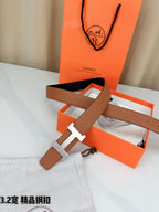 Brown leather belt with gold H buckle and long strap end, shown with buckle centered.