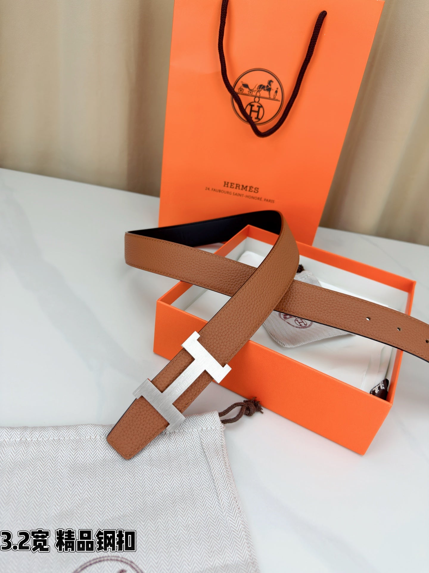 Brown leather belt with gold H buckle and long strap end, shown with buckle centered.