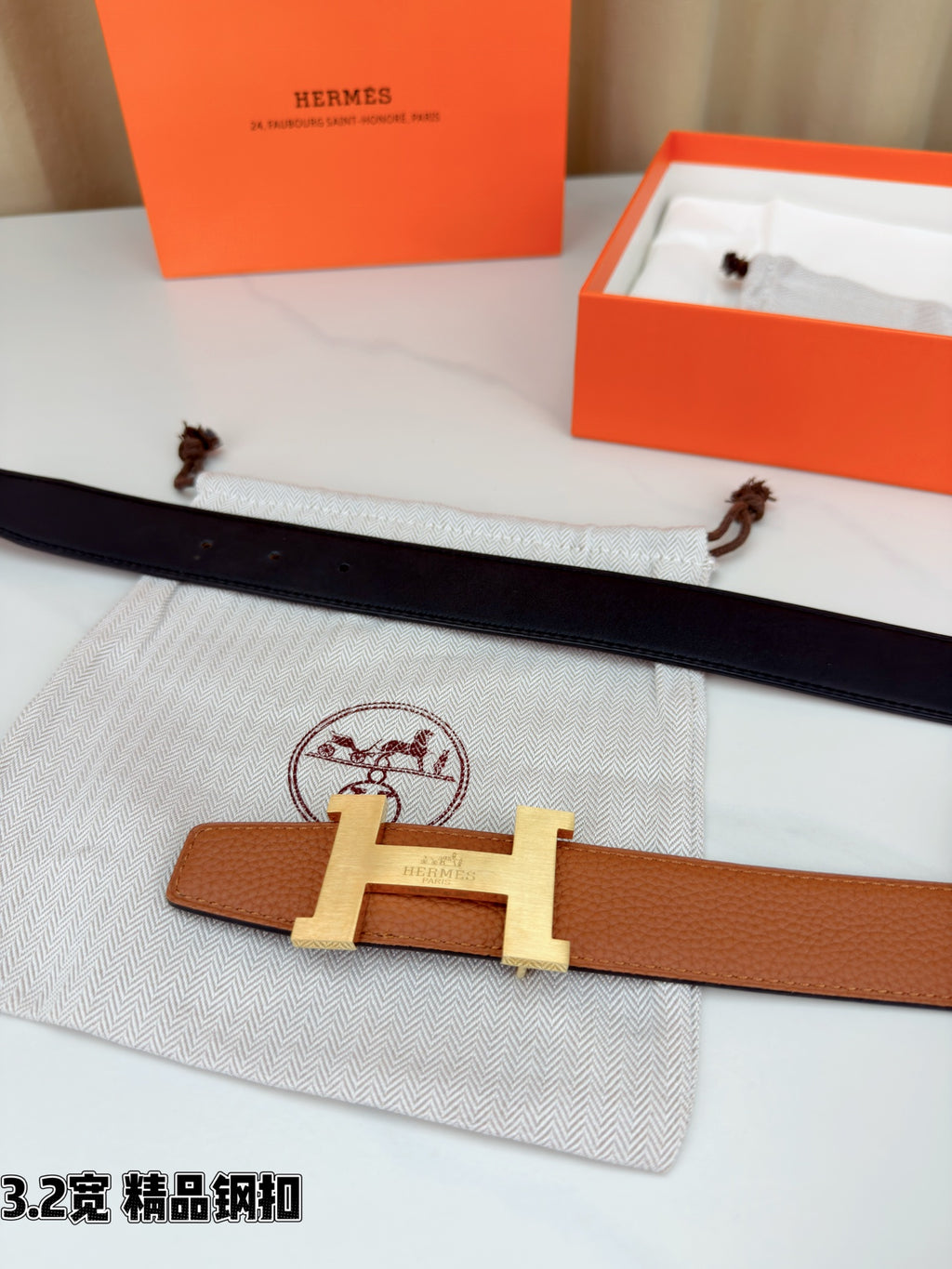 Brown leather belt lying flat with gold H buckle centered and one strap end visible.