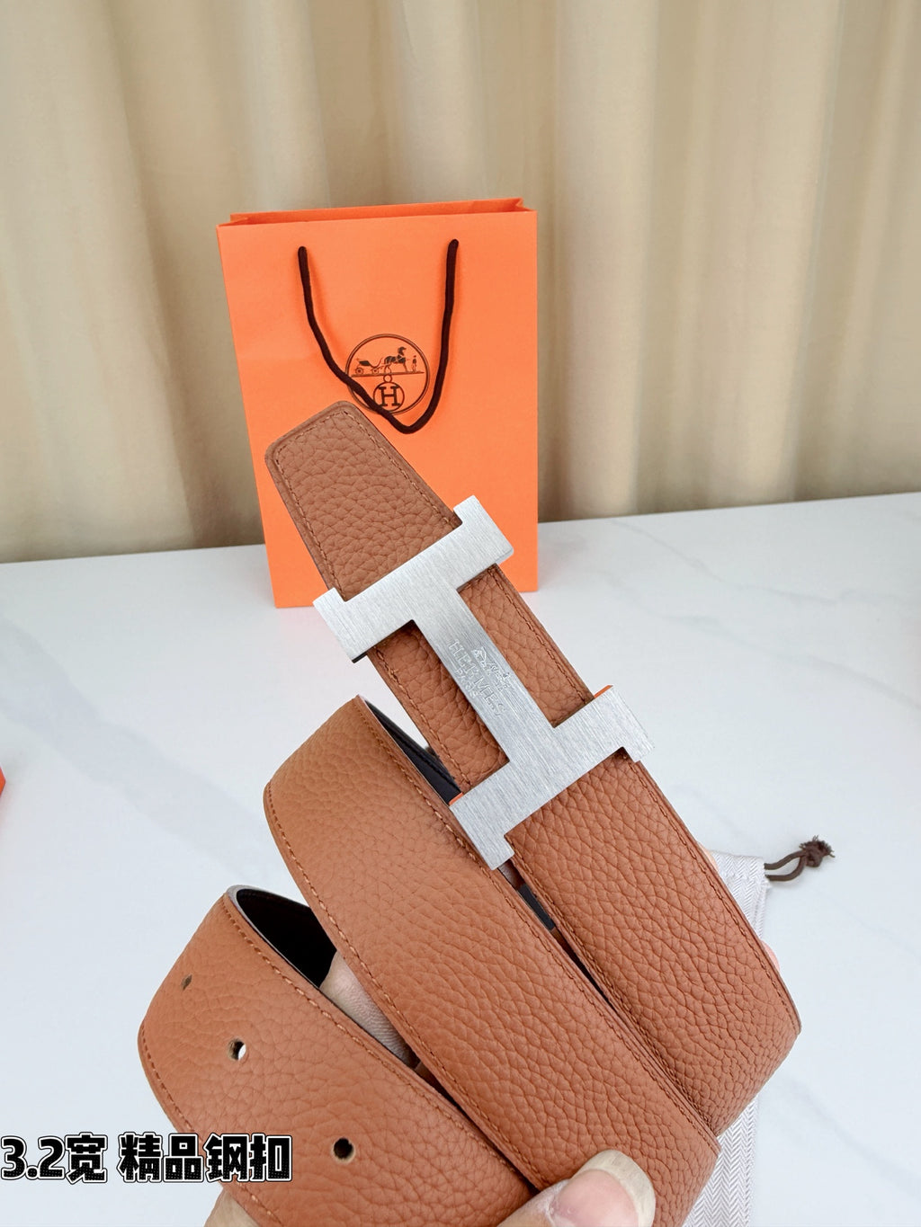 Brown leather belt with gold H buckle and two strap ends, laid in a fan shape.